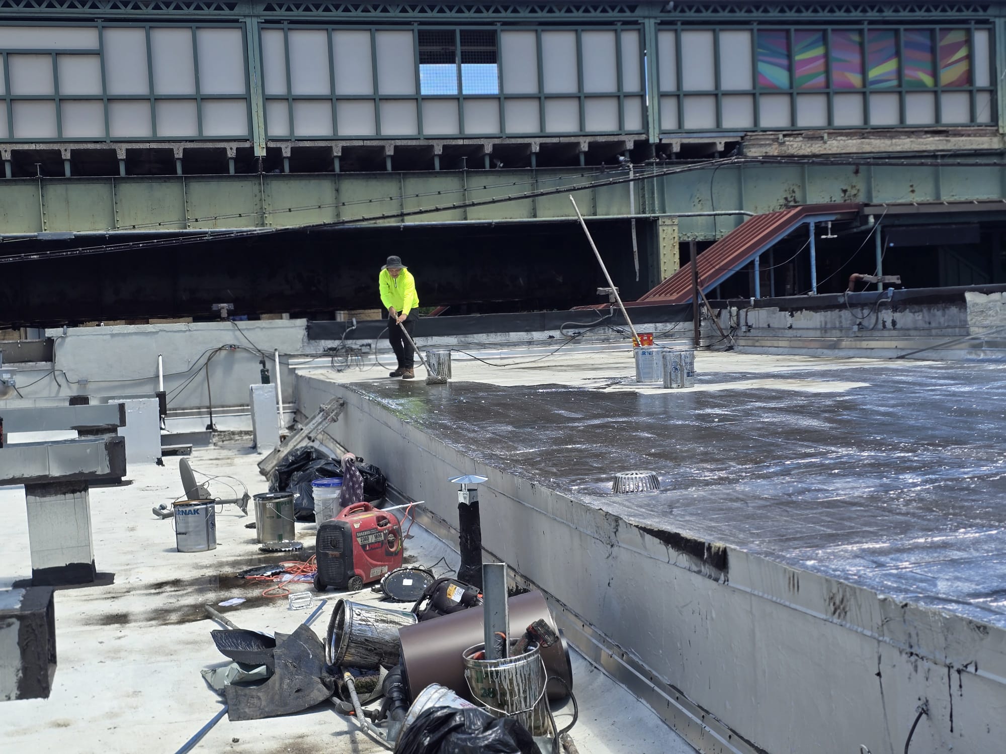 North Star worker in a high-visibility green shirt applying roofing materials on a commercial flat roof